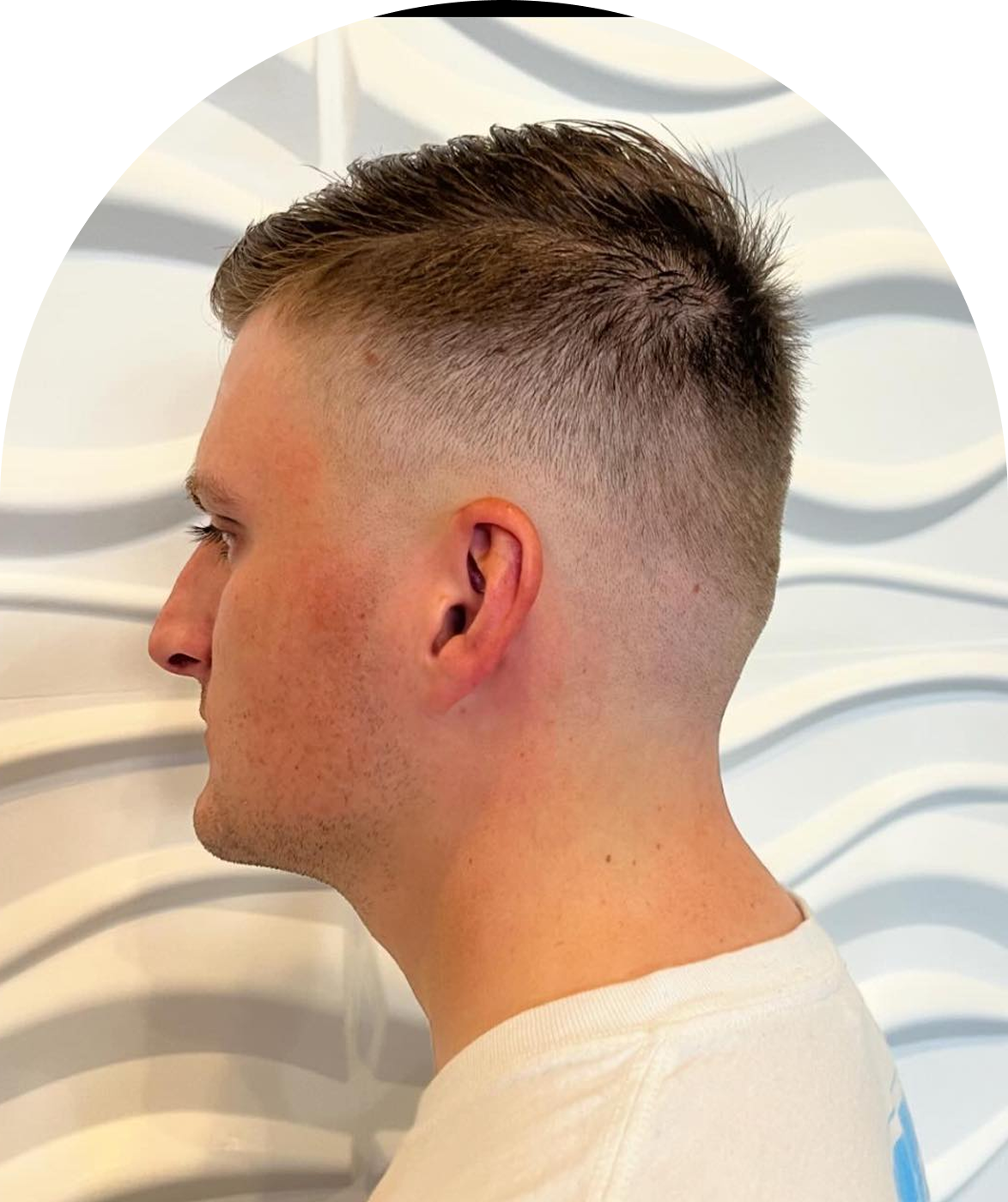 Side profile of a person with a short haircut, featuring a fade on the sides, standing against a patterned background that highlights expertly chosen hair color services.