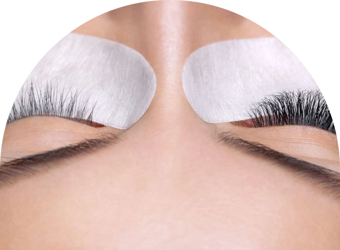 Close-up of a person with closed eyes, wearing under-eye pads, while having eyelash extensions applied. One eye displays natural lashes, the other showcases thick extensions. It's part of their routine beauty ritual, like waxing and hair removal for flawless skin.