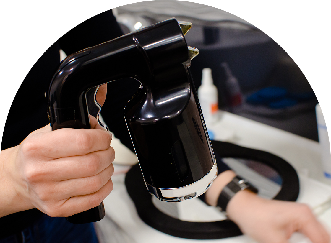 A person grips a sleek, black handheld garment steamer with precision, their other hand reaching toward a black fabric item on the table, reminiscent of the careful approach one might take during waxing and hair removal.