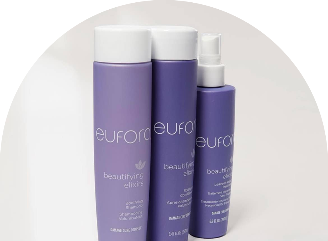 Three purple bottles of Eufora beautifying elixirs, perfect for complementing any hair color services, include a Bodyfying Shampoo, Conditioner, and Leave-In Repair Treatment. They are elegantly displayed against a pristine white background.